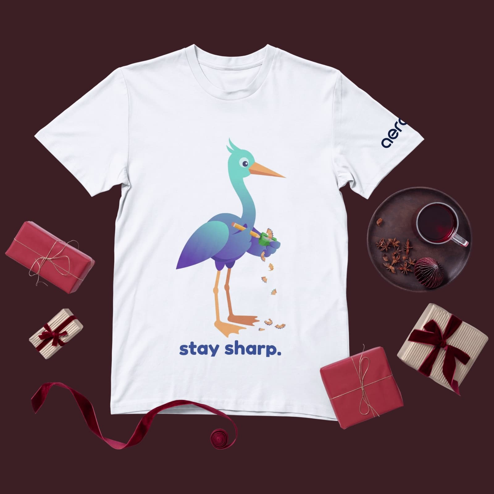 White tee printed with the heron sharpening a pencil, shavings falling, above the words stay sharp